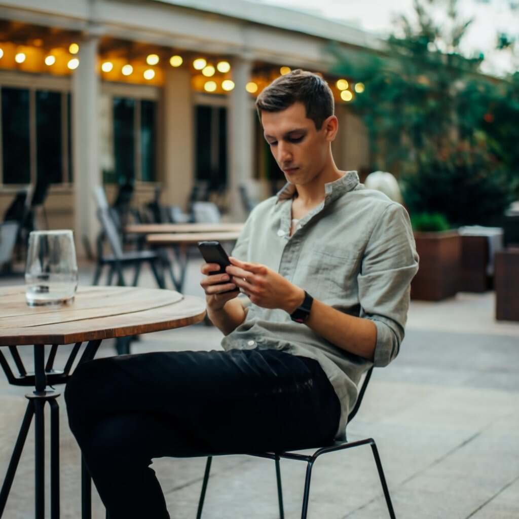 A man sitting at a table looking at his phone - Engaging with Tinder profiles.
